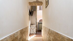 Un pasillo estrecho con suelo de madera, un radiador y una puerta que da a una habitación con ventana.