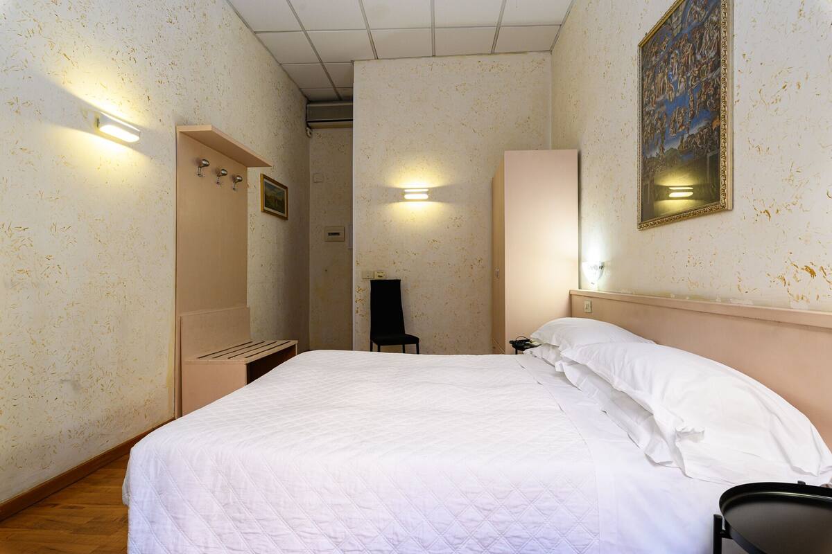 Habitació d'hotel amb un llit gran, una cadira, un armari i un quadre a la paret.