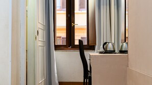 Un pasillo estrecho con una puerta que da a un balcón. Hay una silla y una mesa con dos pitarros encima.