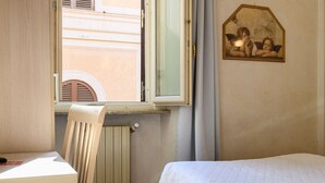 Un dormitorio con cama, una silla, un radiador, una ventana y un cuadro colgado en la pared.