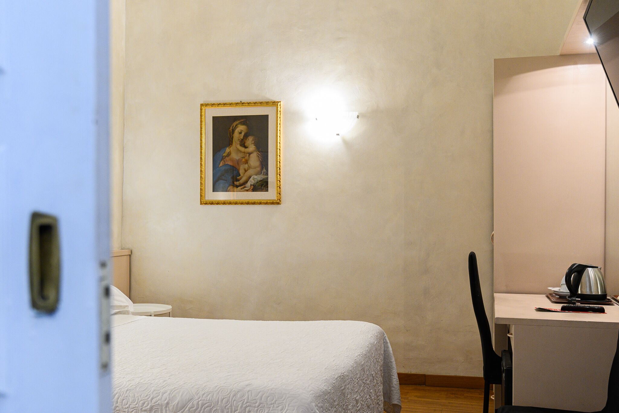 Una habitación de hotel con cama, escritorio con hervidor y un cuadro en la pared.