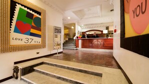 Un hall d’hôtel comprenant un comptoir d’accueil, un escalier et une œuvre d’art murale aux couleurs vives.