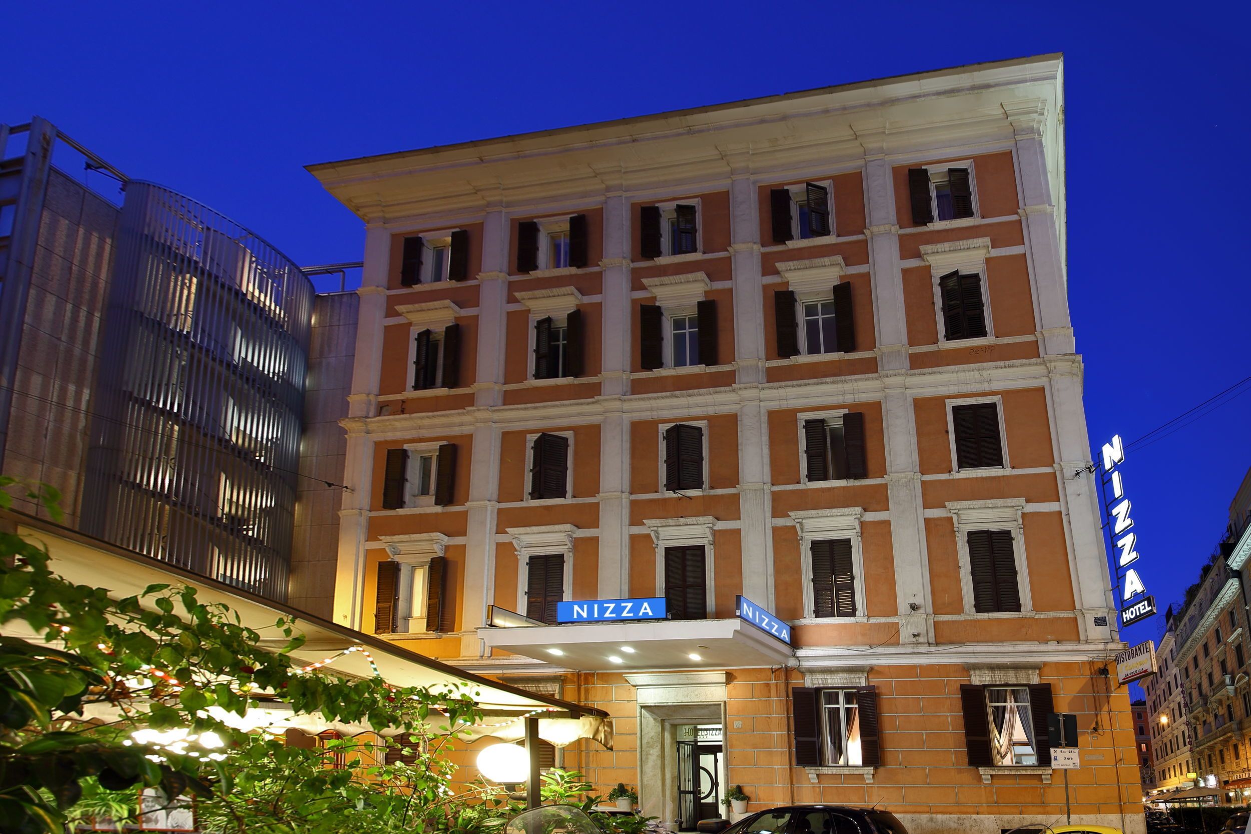 A multi-story hotel with a prominent 'Nizza' sign, featuring a classic architectural style with columns and a balcony.