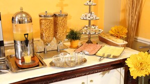 Un buffet comprenant un distributeur de jus, des récipients à céréales, un présentoir à plusieurs niveaux pour les desserts et un arrangement floral en guise de décoration centrale.