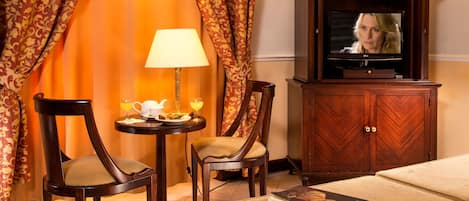 Habitación de hotel con televisión, dos sillas, una mesa con lámpara y una cama.