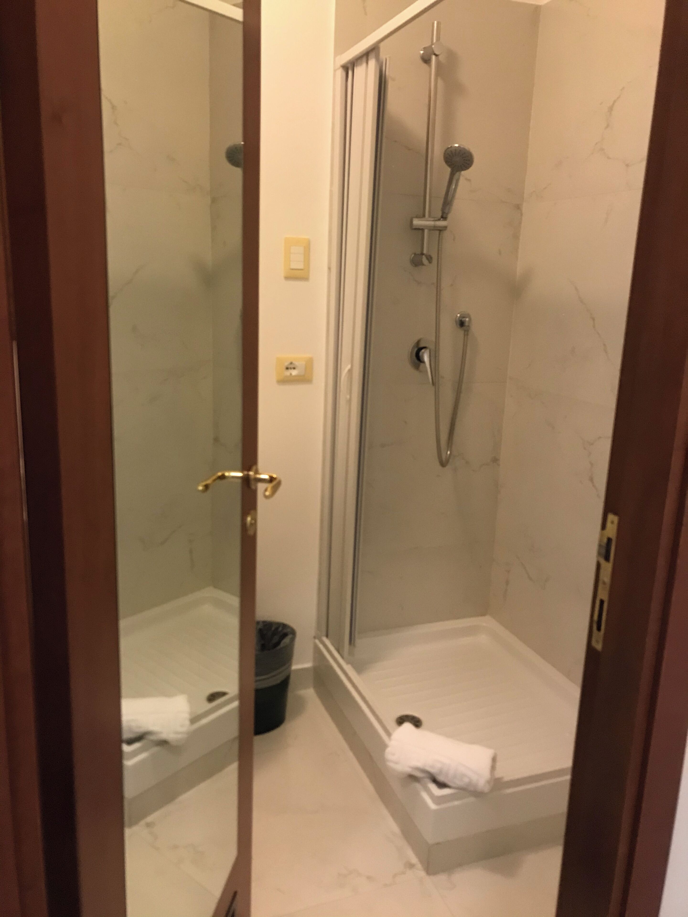 A glass-enclosed shower area with a white marble wall, a towel on the floor, and a trash bin.