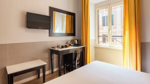A hotel room with a bed, a desk with a chair, a small table, a TV mounted on the wall, and a window with yellow curtains. - Hotel Virgilio (Rome)
