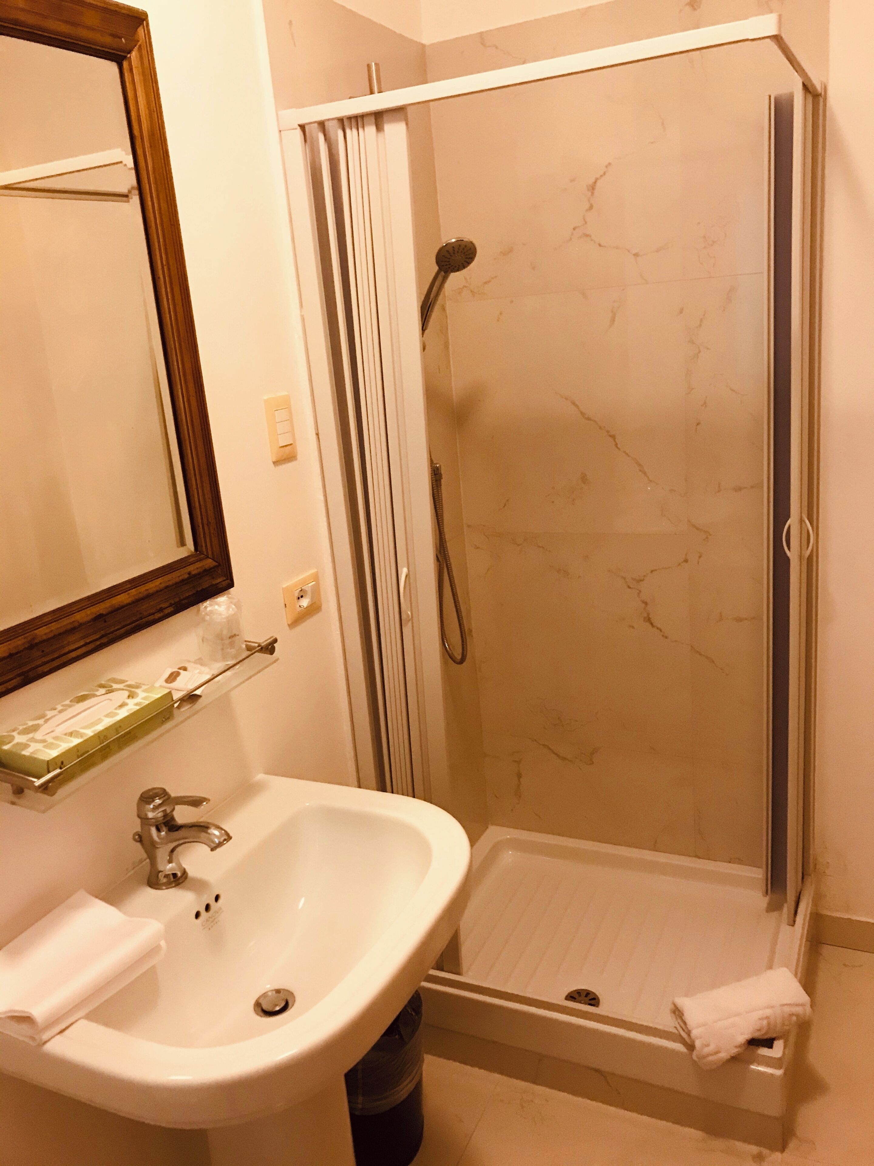A bathroom with a sink, mirror, shower, and towel rack.
