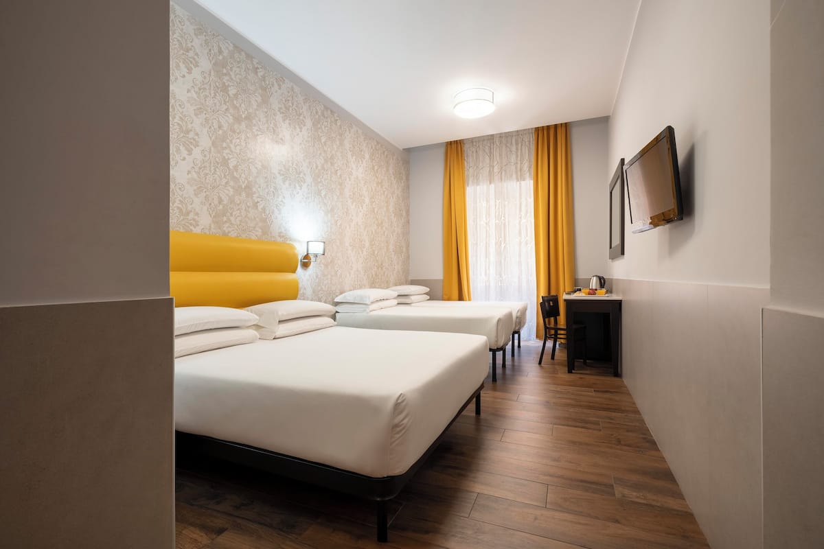 Hotellihuone, jossa on kaksi sänkyä, työpöytä, tuoli, televisio ja ikkuna, jossa on verhot.