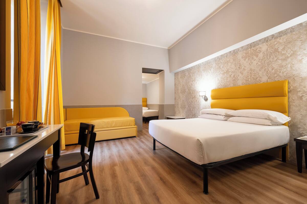 Hotellihuone, jossa on sänky, työpöytä, tuoli, sohva ja pieni pöytä.