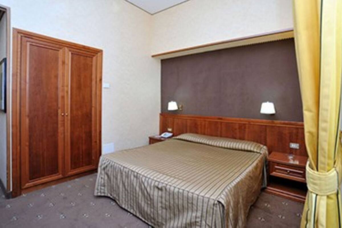 Hotellihuone, jossa on sänky, yöpöytä, puinen vaatekaappi ja sängynpääty.