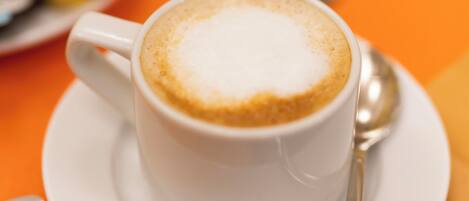 A cup of coffee on a white saucer with a spoon, on an orange table.
