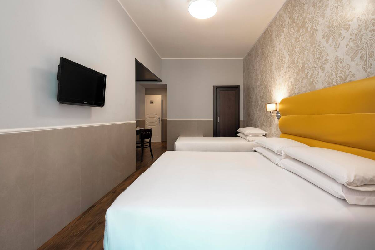 Hotellihuone, jossa on sänky, seinälle asennettu televisio, työpöytä tuolilla ja ovi.