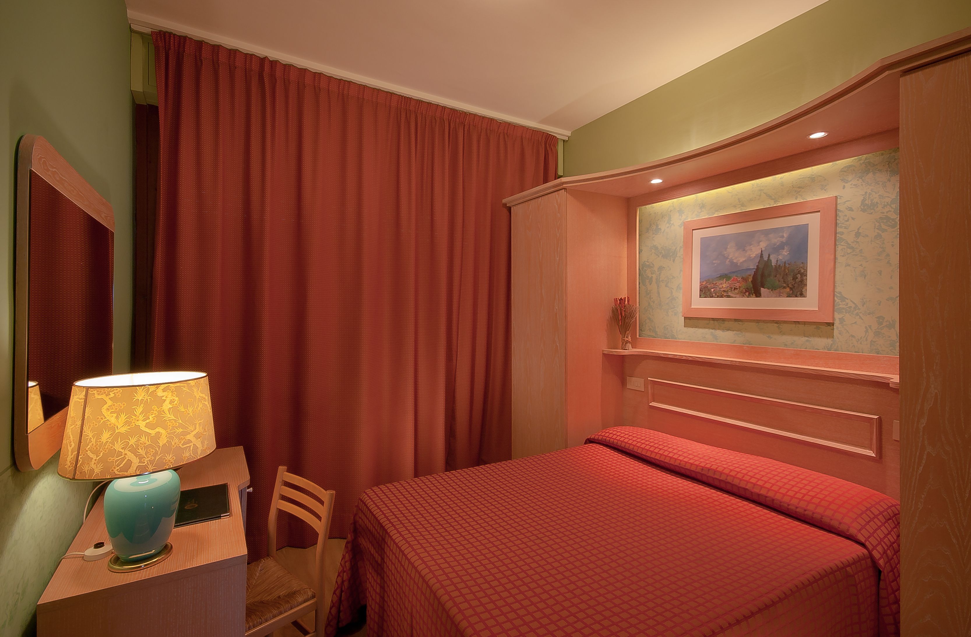 Una habitación de hotel con una cama, un escritorio con lámpara, una silla y un cuadro en la pared.
