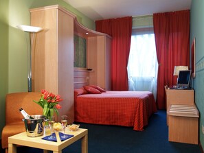 Una habitación de hotel con cama, un escritorio con una botella de champán, copas y un jarrón de flores.
