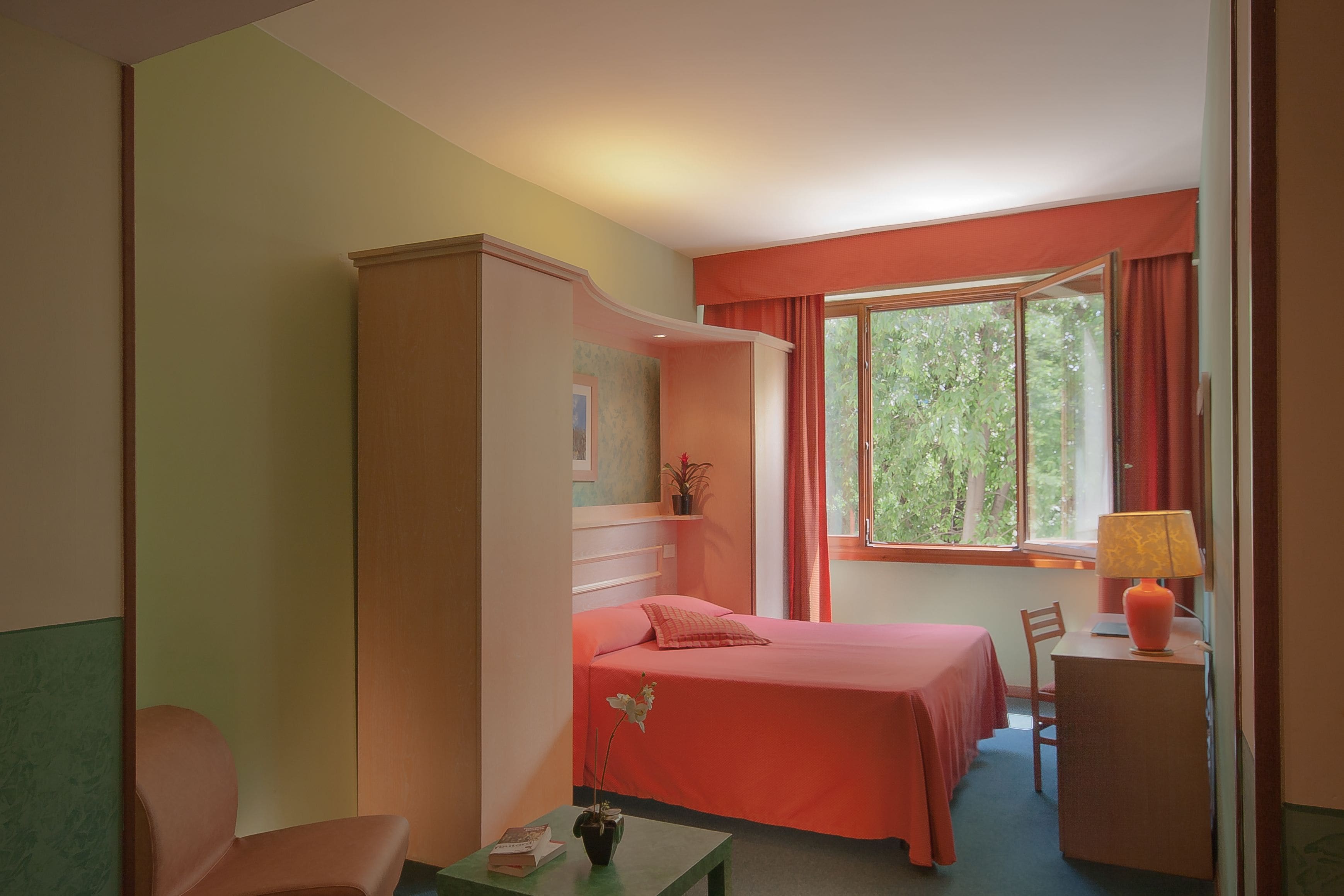 A bedroom with a bed, a desk, a chair, a wardrobe, and a window with curtains.
