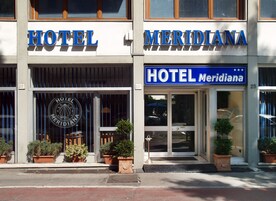 Un hotel llamado "Meridiana" con un gran letrero sobre la entrada, plantas en macetas en la parte delantera y el número visible "23".