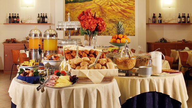 A breakfast buffet with various food items and beverages, a painting on the wall, and wine bottles on shelves. - Hotel Meridiana (Florence)