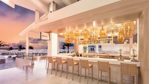 Un espace bar avec des fauteuils en osier et des luminaires suspendus, donnant sur une plage.