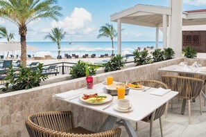 A beachside dining area with outdoor seating, a view of the ocean, and a covered patio. - Starfish Halcyon Cove Resort Antigua - All Inclusive (St. John's)