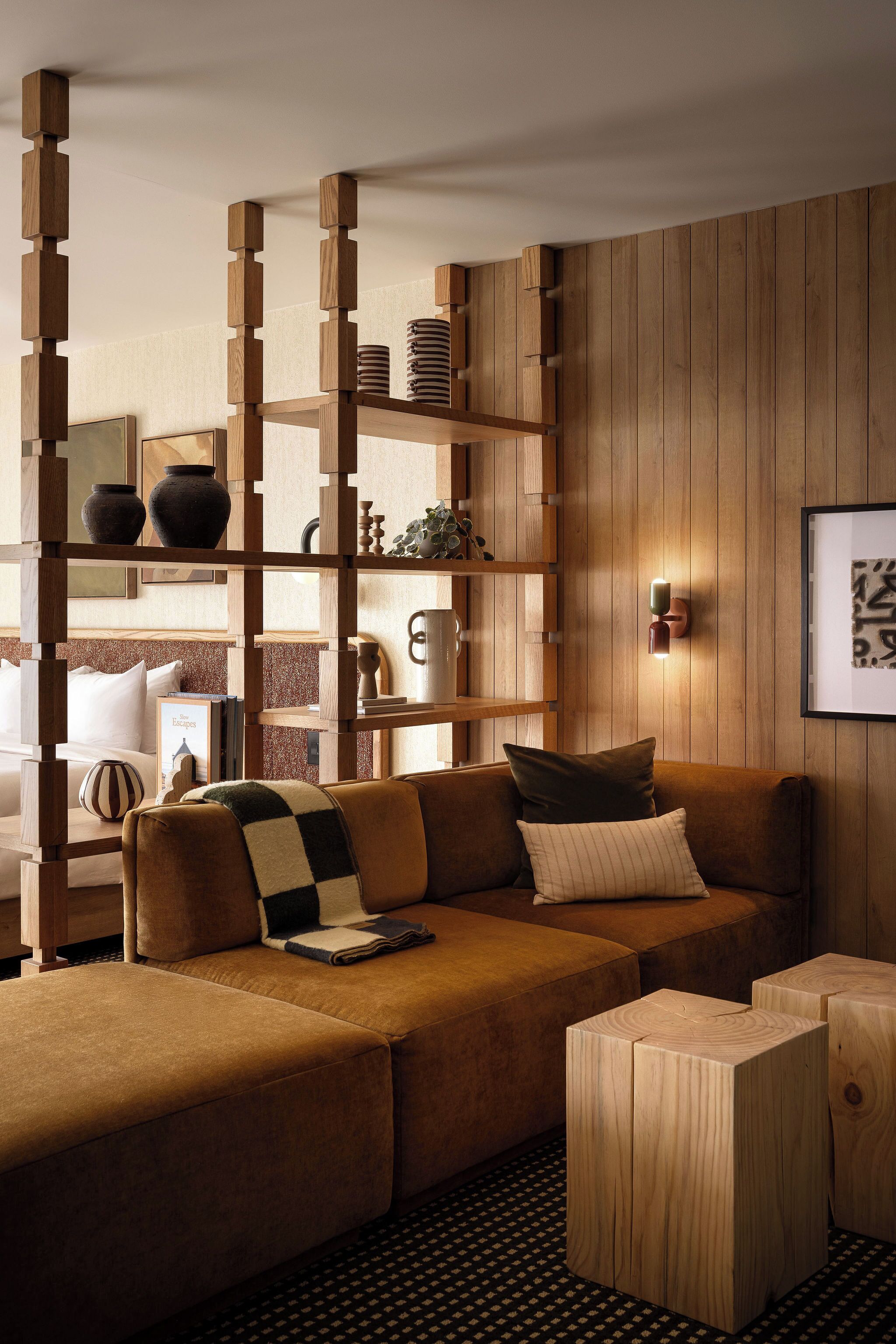 Una sala moderna con un sofá marrón, mesitas de madera y una estantería de madera decorada con objetos.
