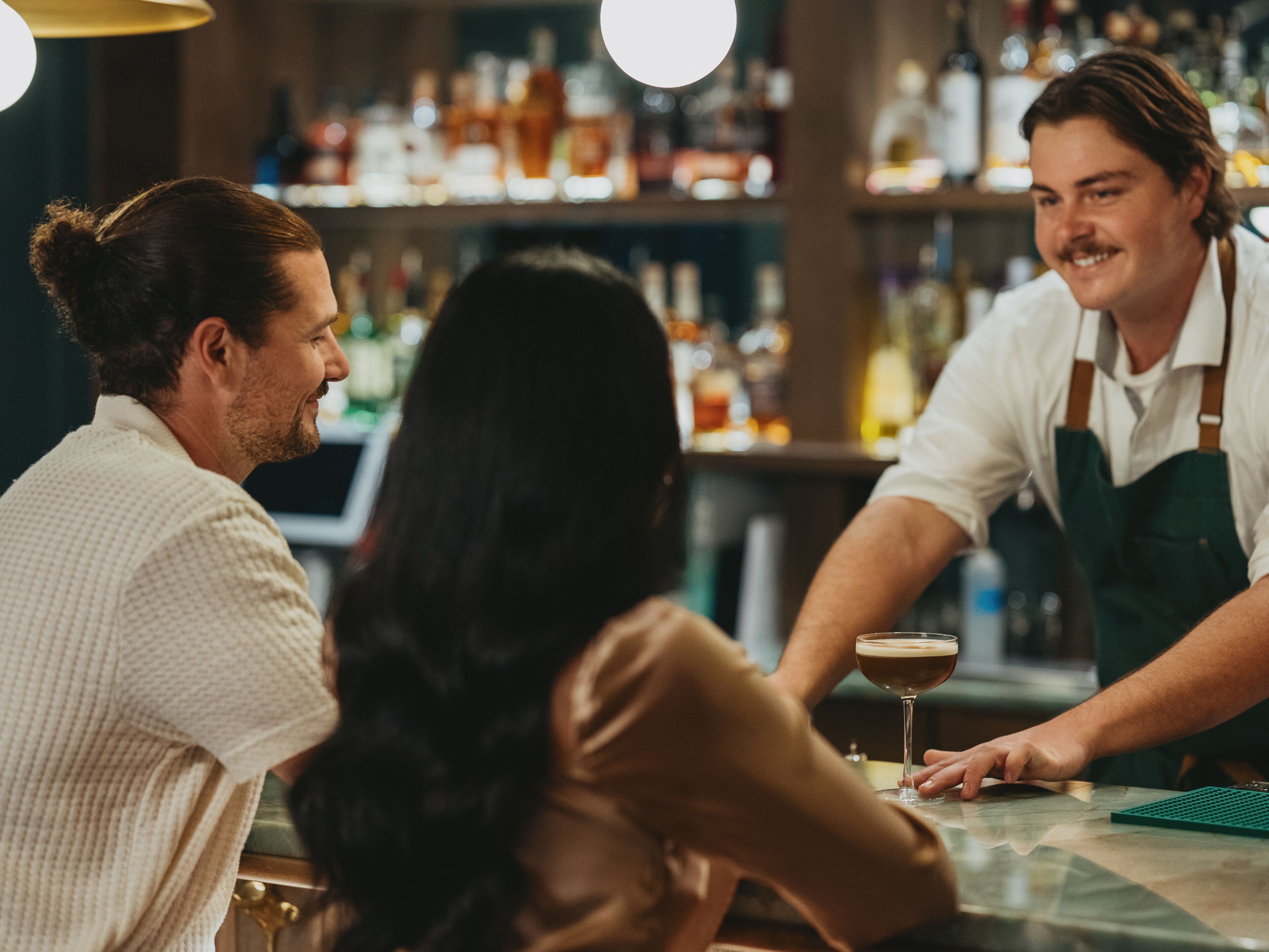 Un bar avec un barman et deux clients.