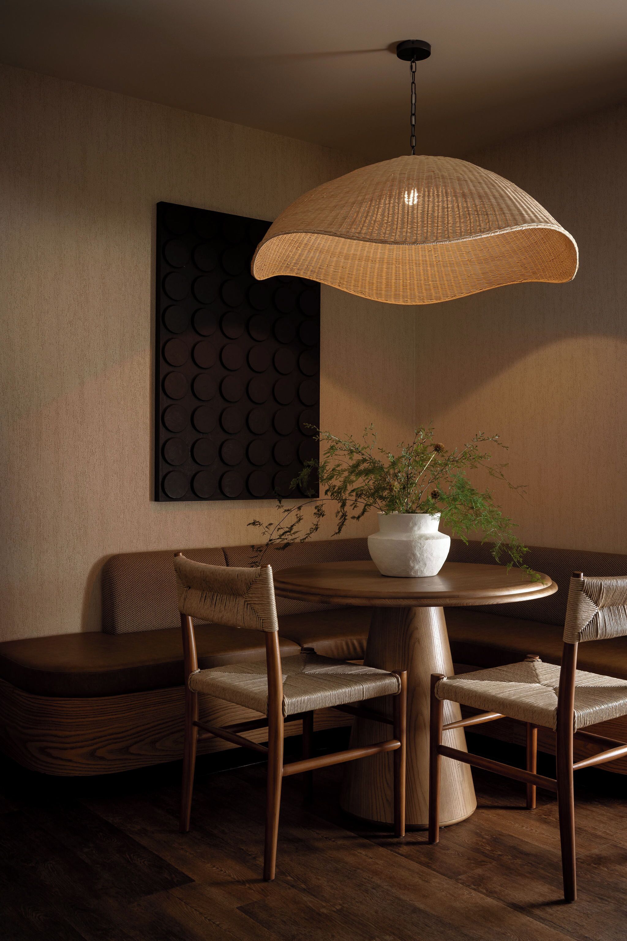 A dining area with a round table, four chairs, a hanging light fixture, and a potted plant.