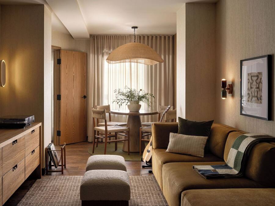A modern living room with a sofa, ottoman, dining table, chairs, and a television.