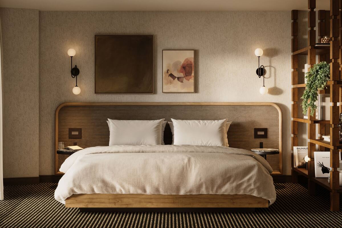 A modern hotel room with a large bed, a wooden headboard, two wall-mounted light fixtures, and a decorative wall piece.