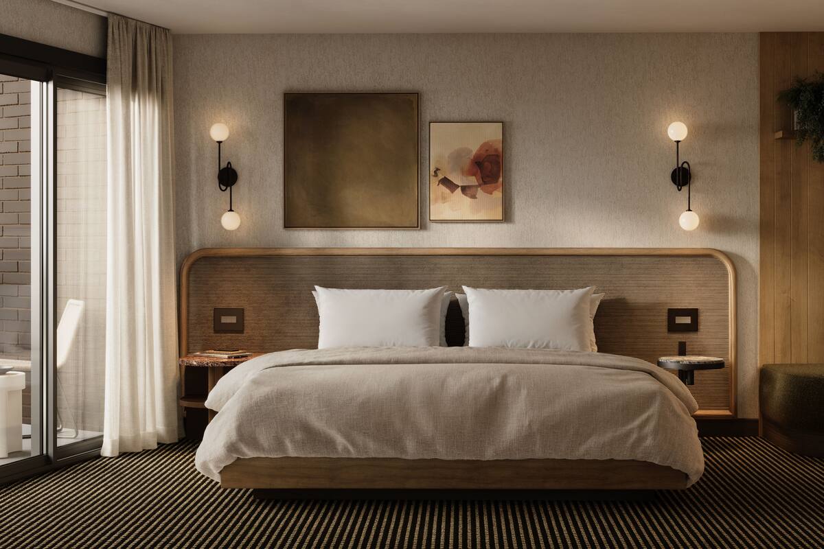 A modern hotel room with a large bed, two bedside tables, a headboard with a wooden finish, a large window with curtains, and wall-mounted lighting.