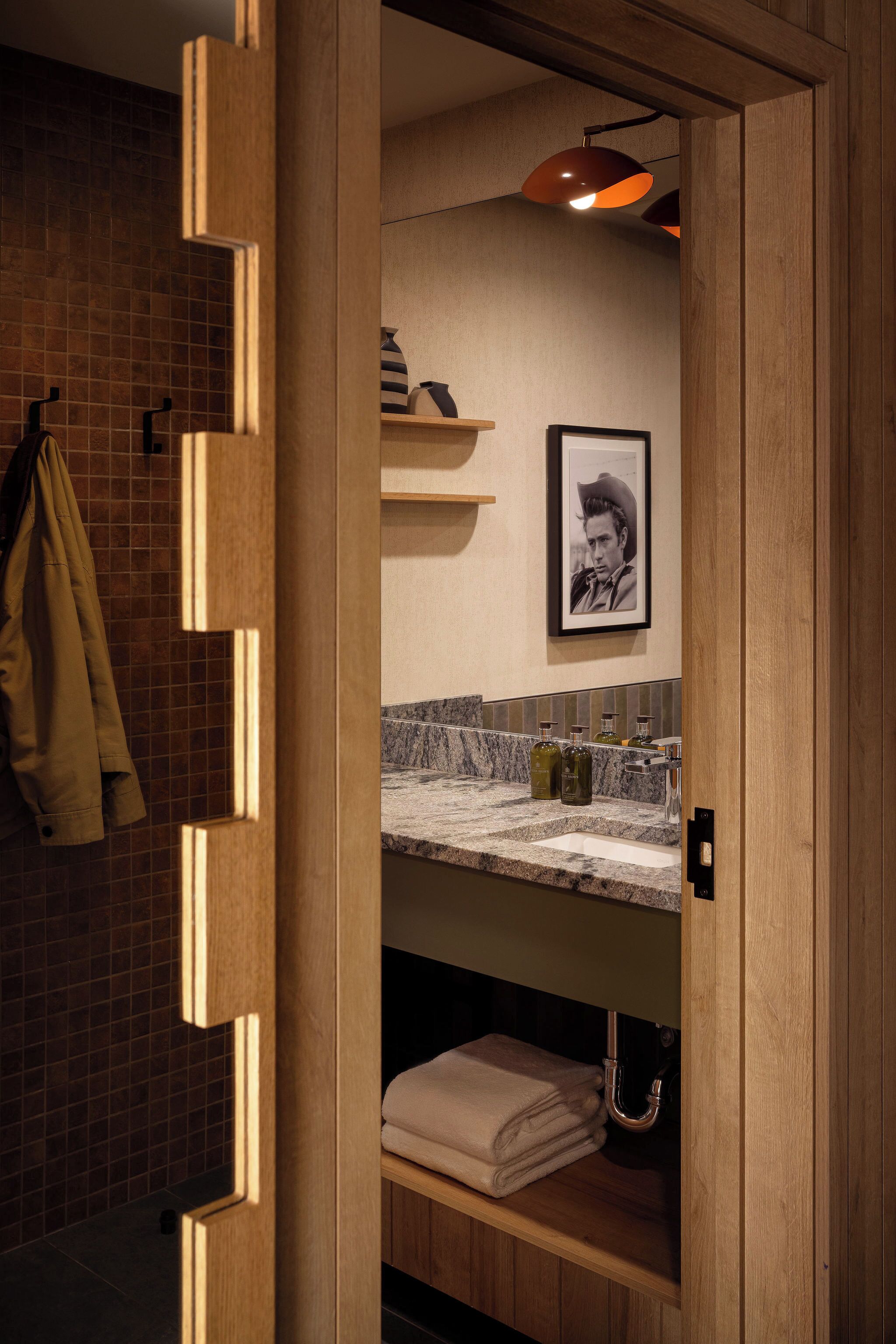 A modern bathroom with a wooden vanity, a towel rack, a framed picture, and a marble countertop.