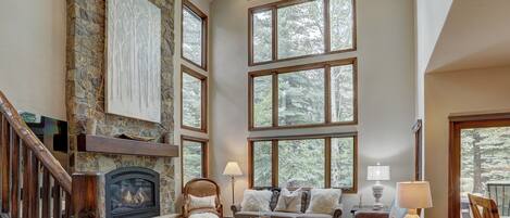 A spacious living room with a stone fireplace, large windows, and a cozy seating area.