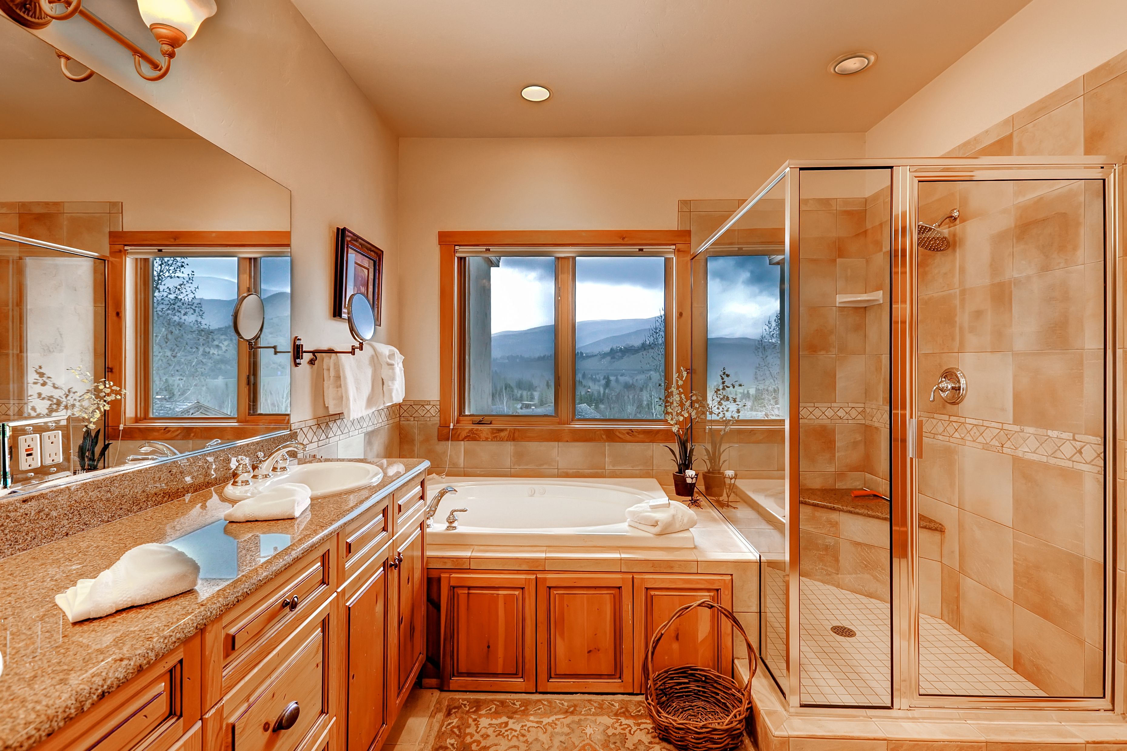 A spacious bathroom with a large bathtub, a walk-in shower, and a view of mountains through the windows.
