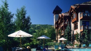 A pool area with lounge chairs and umbrellas, surrounded by a building with balconies and a view of a hilly landscape. - Arrowhead Village, A Vail Resorts Property (Edwards)