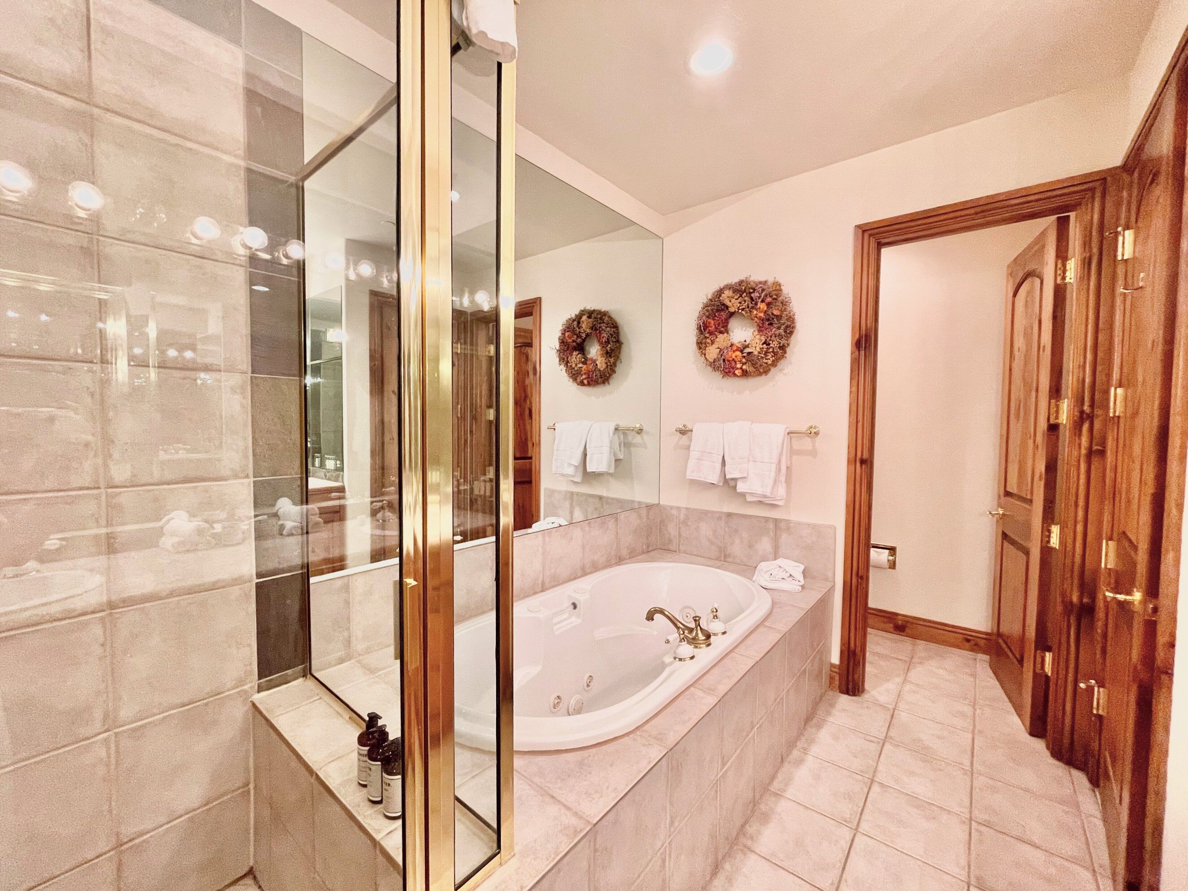A modern bathroom with a glass-enclosed shower, a freestanding bathtub, and a wooden door.