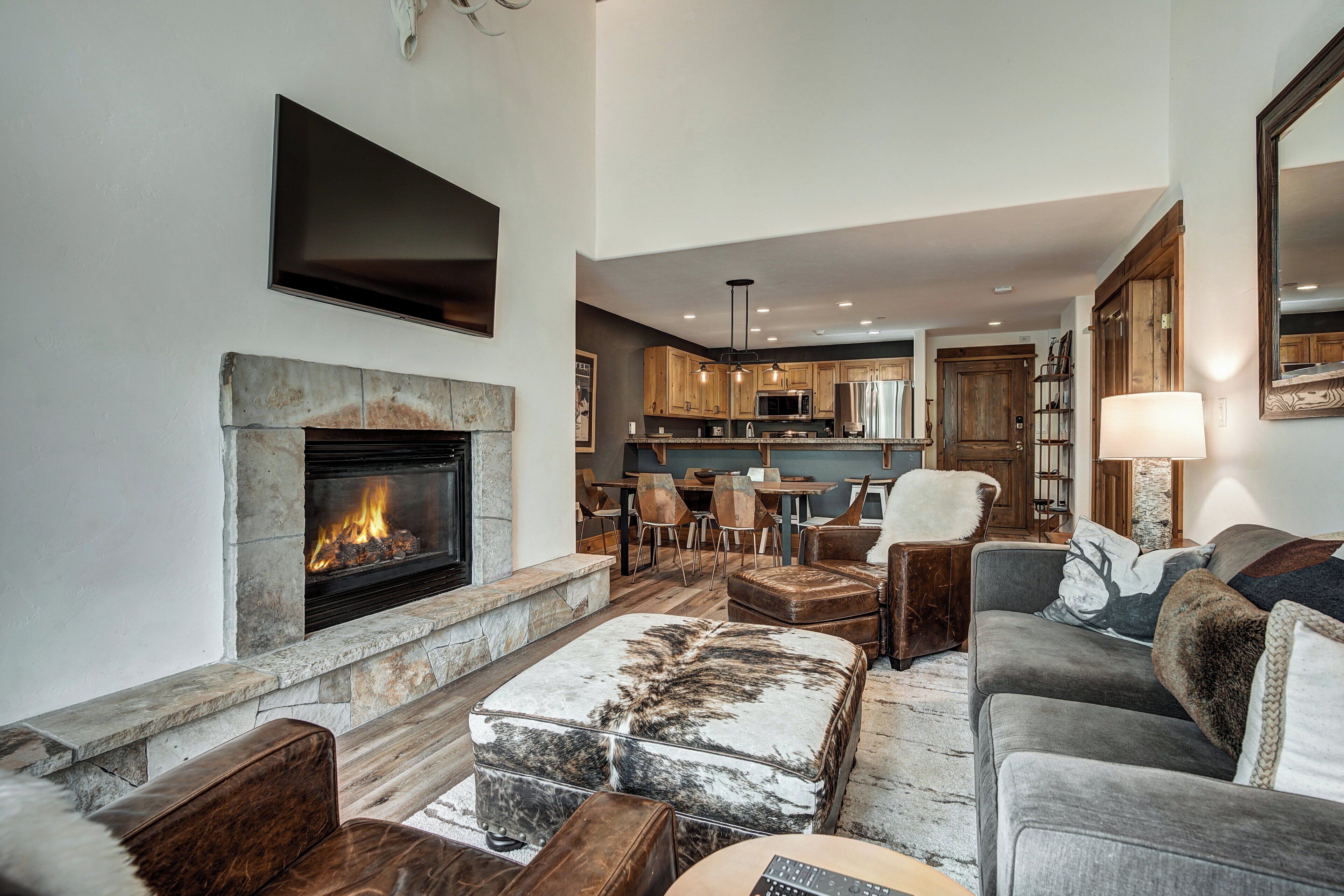 A modern living room with a fireplace, comfortable seating, and a kitchen in the background.