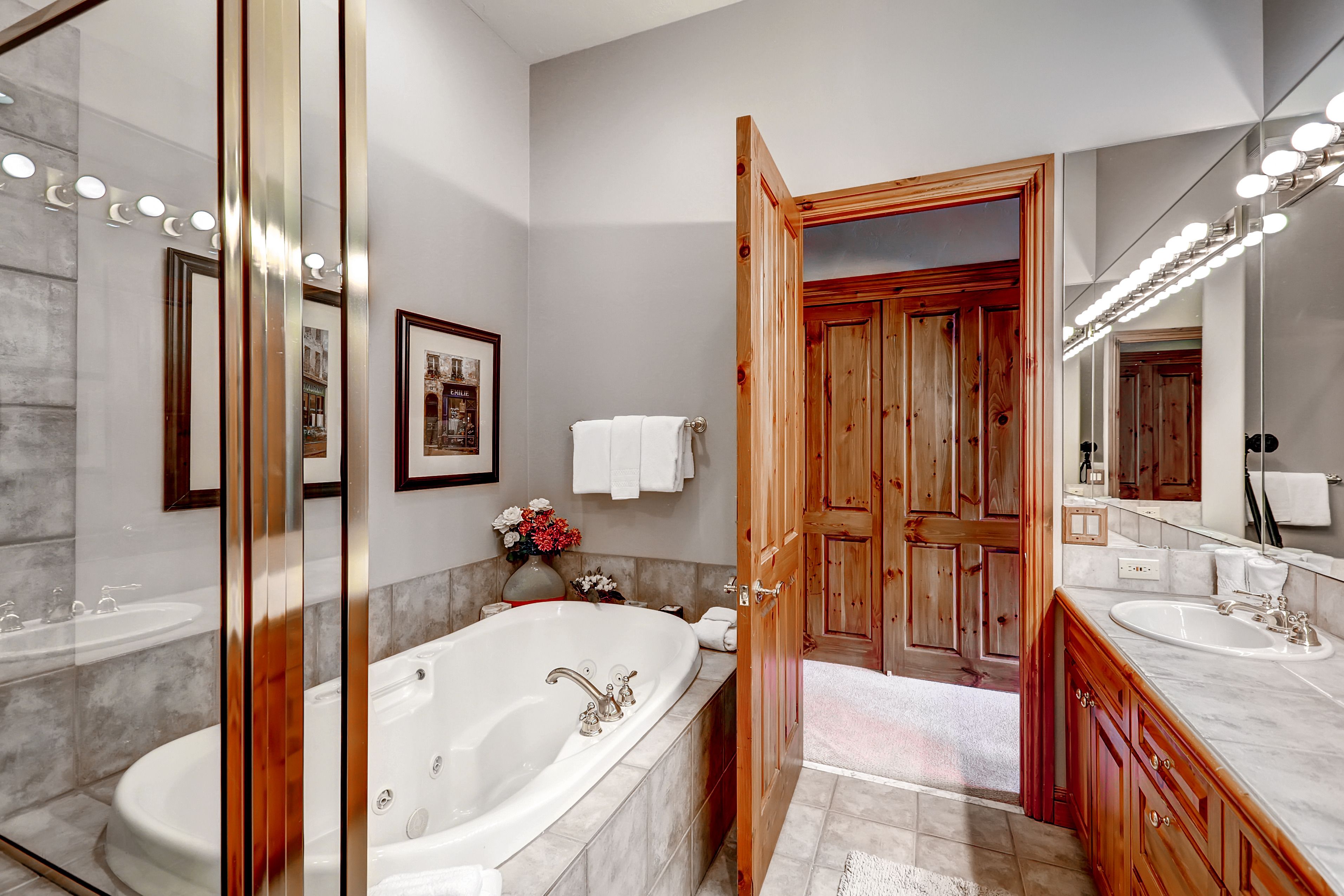 A modern bathroom with a large bathtub, wooden vanity, and a mirror with lights.