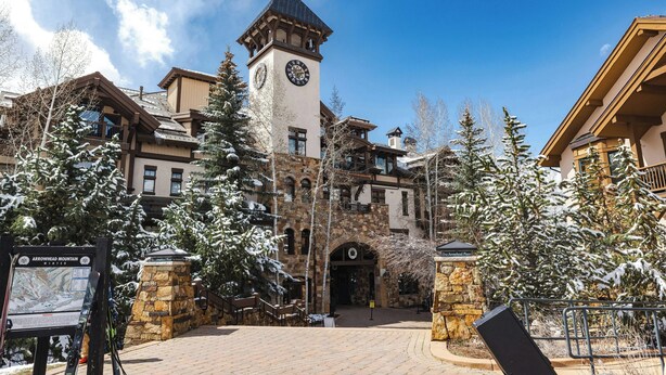 A historic building with a clock tower, stone architecture, and snow-covered trees. - Arrowhead Village, A Vail Resorts Property (Edwards)