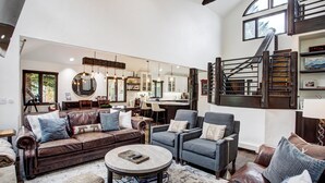 A spacious living room with a leather sofa, armchairs, and a coffee table. A staircase with a wooden railing leads to an upper level. - Arrowhead Village, A Vail Resorts Property (Edwards)