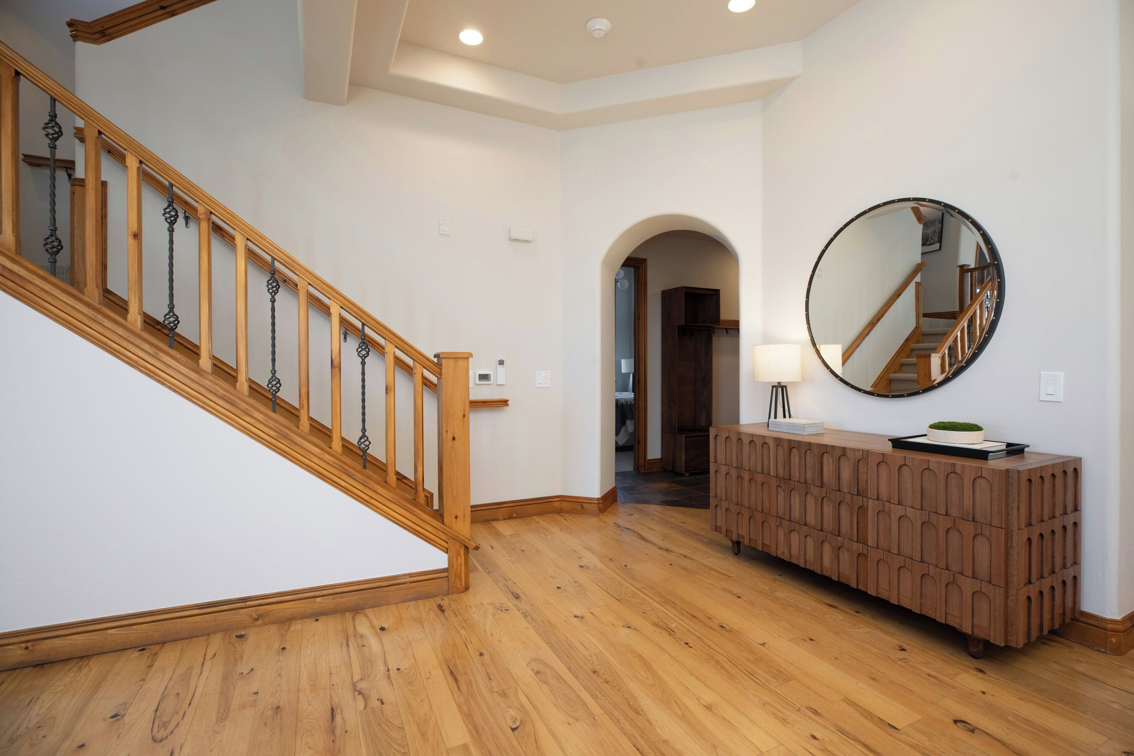 Un escalier en bois avec une rampe, un miroir rond accroché au mur et un meuble en bois.