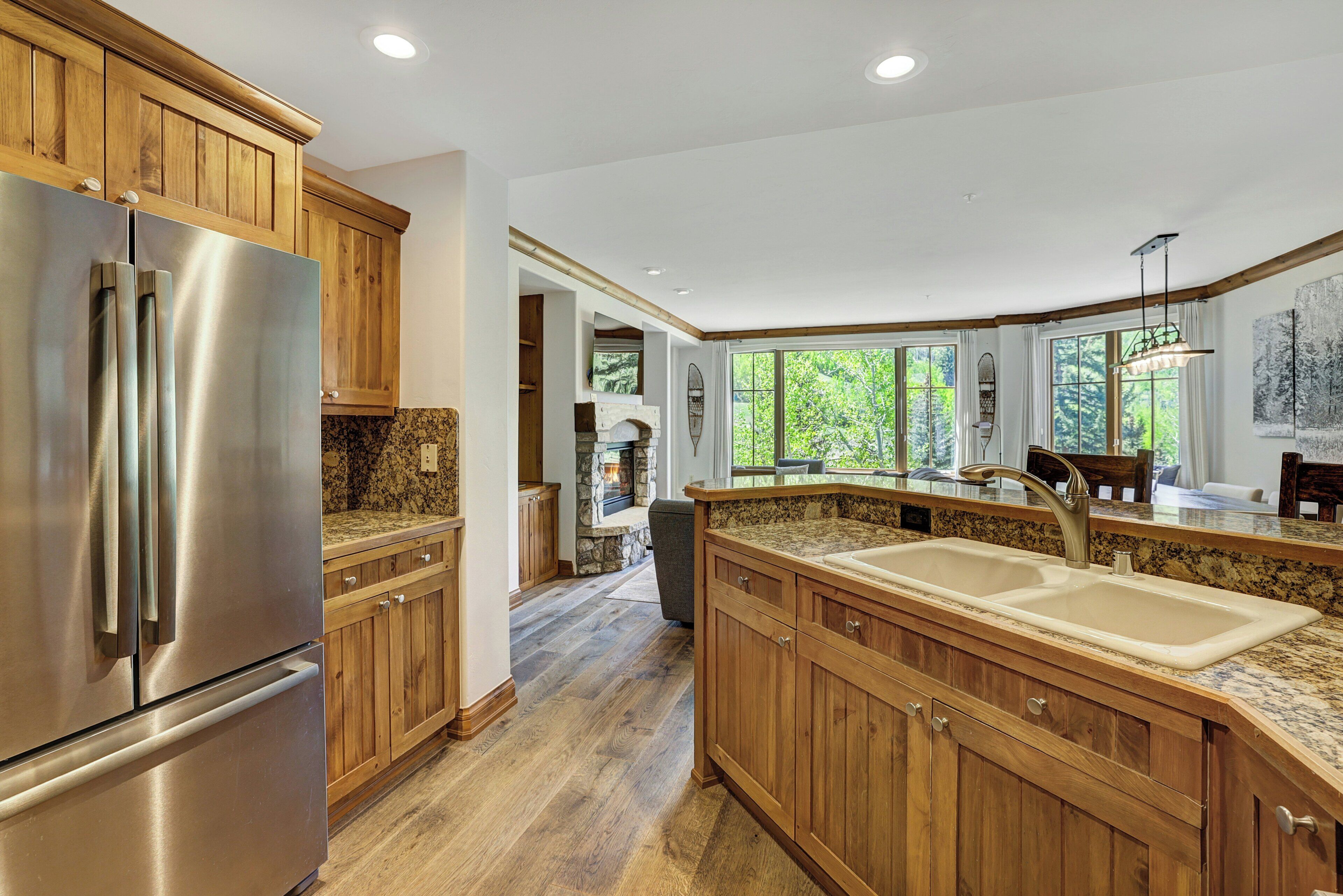Een keuken met houten kastjes, een roestvrijstalen koelkast, granieten aanrechtbladen en een grote gootsteen.