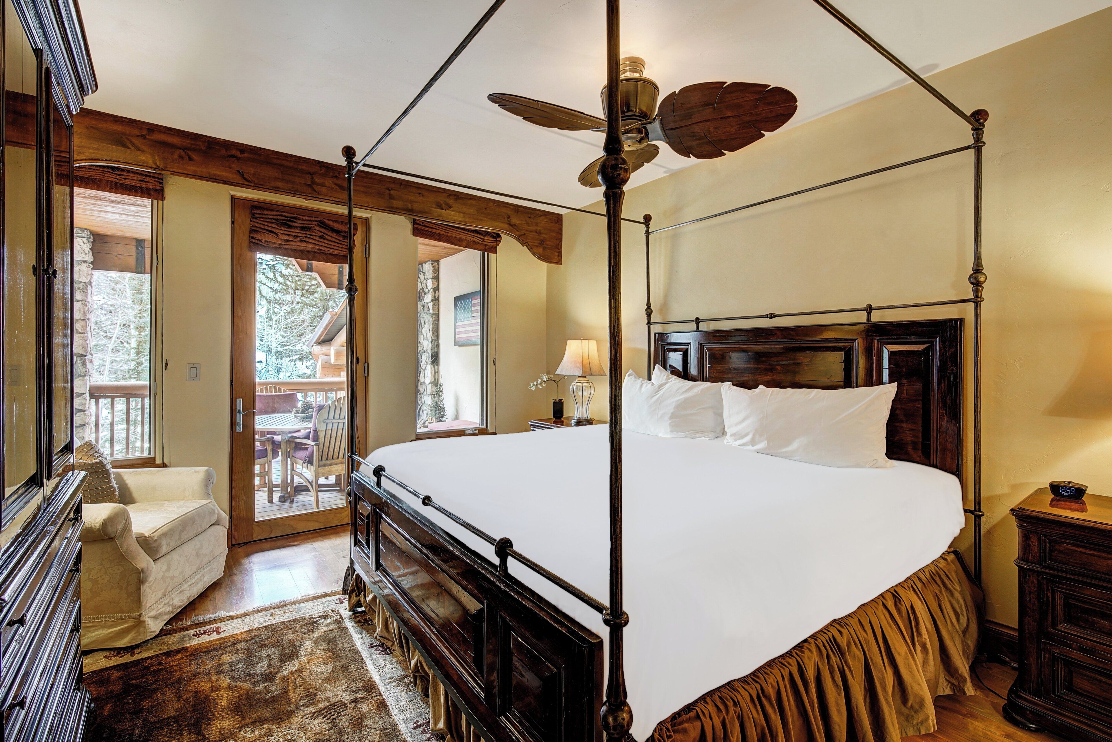 A four-poster bed with a wooden headboard, a ceiling fan, and a view of the outdoors through a glass door.
