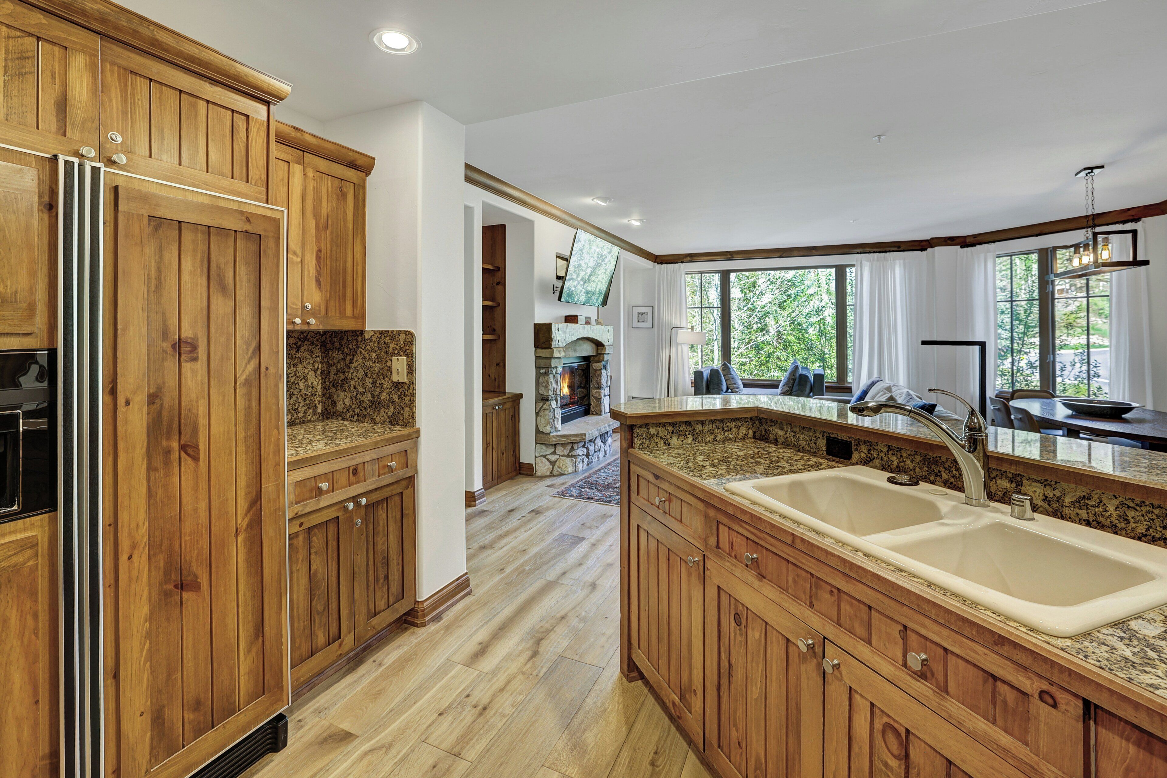 A kitchen with wooden cabinets, granite countertops, a double sink, and a stone fireplace.
