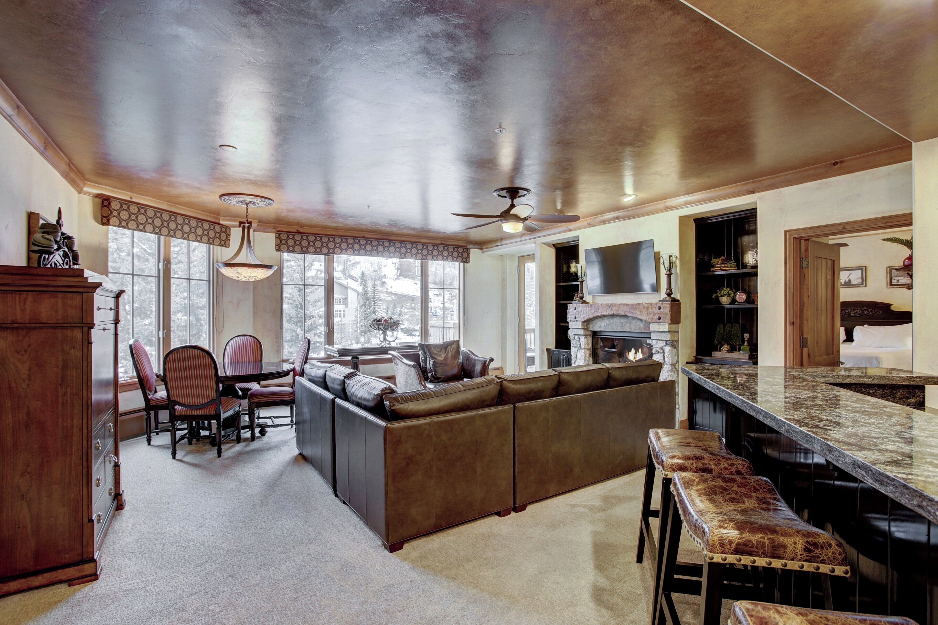 A spacious living area with a large sectional sofa, a dining table with chairs, a bar area with stools, and a fireplace.