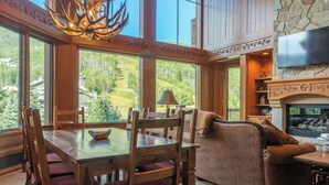 A spacious living area with a large wooden dining table, comfortable seating, a fireplace, and a television mounted on a stone wall. - Elkhorn Lodge, A Vail Resorts Property (Avon)