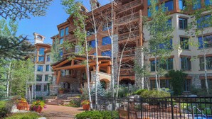 A multi-story hotel with a stone facade, multiple balconies, and a landscaped courtyard with pathways and potted plants. - Elkhorn Lodge, A Vail Resorts Property (Avon)
