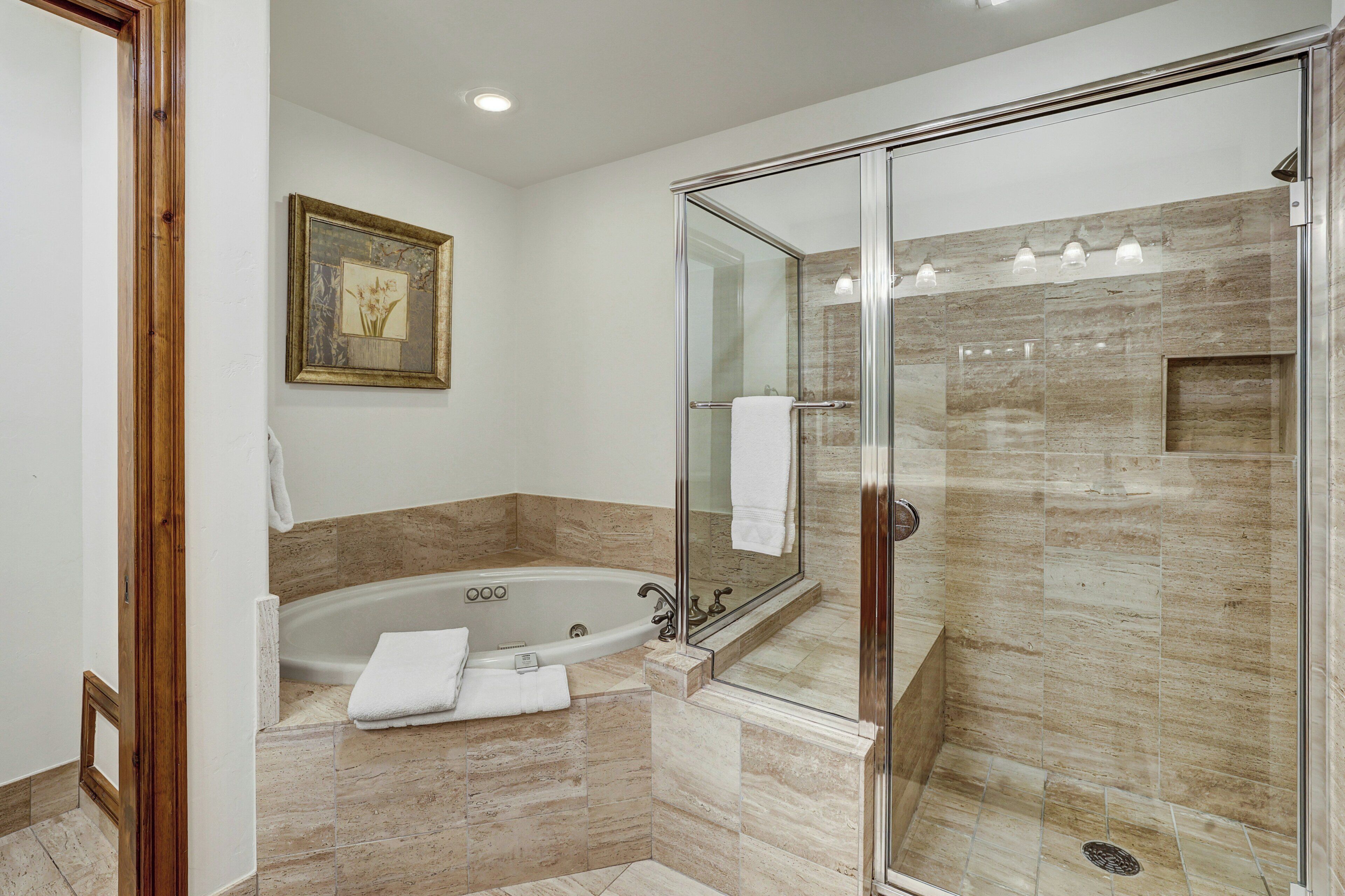 A modern bathroom with a glass-enclosed shower, a freestanding bathtub, and a marble-tiled floor.