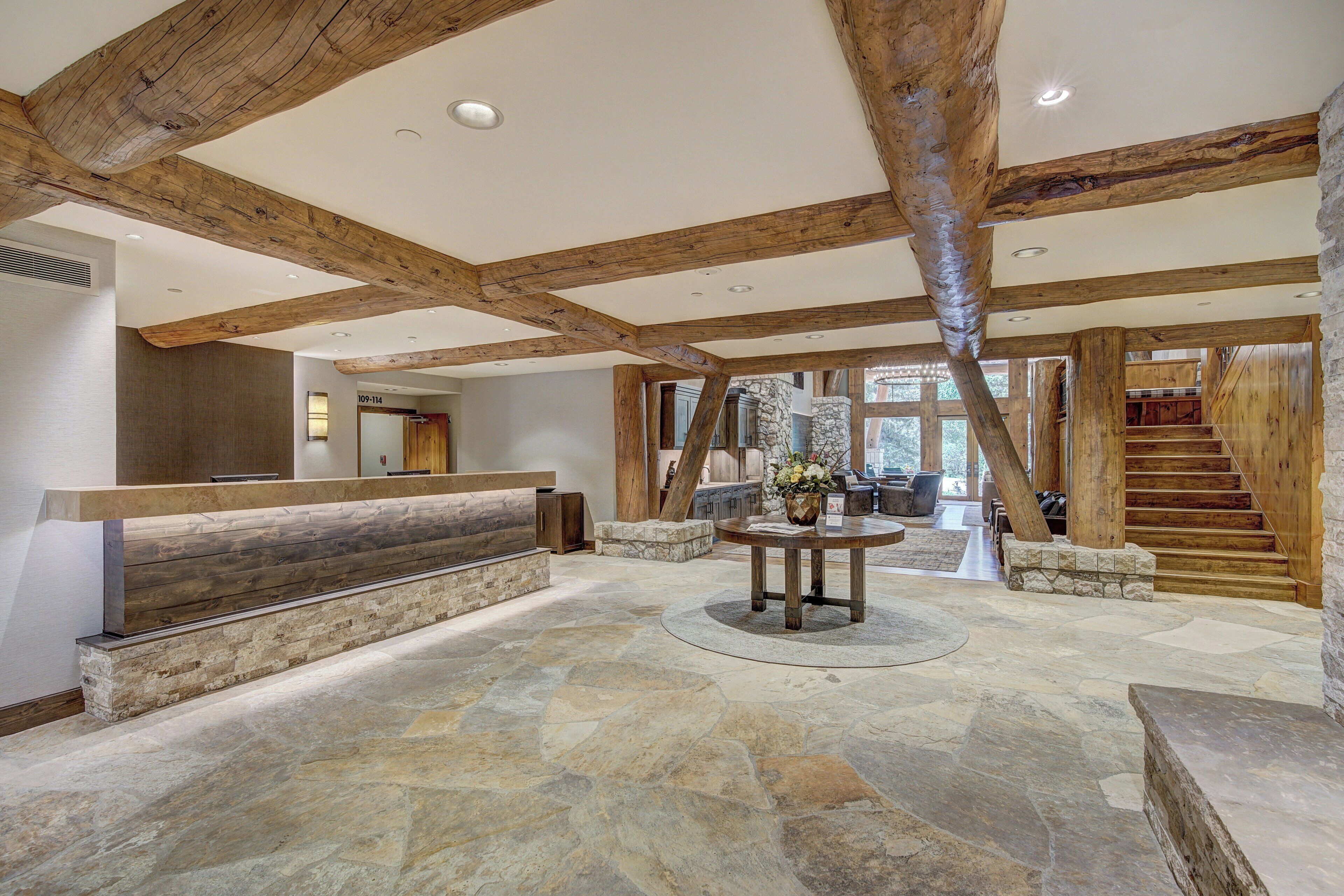 A spacious lobby with a stone floor, wooden beams, a reception desk, and a staircase leading to upper levels.