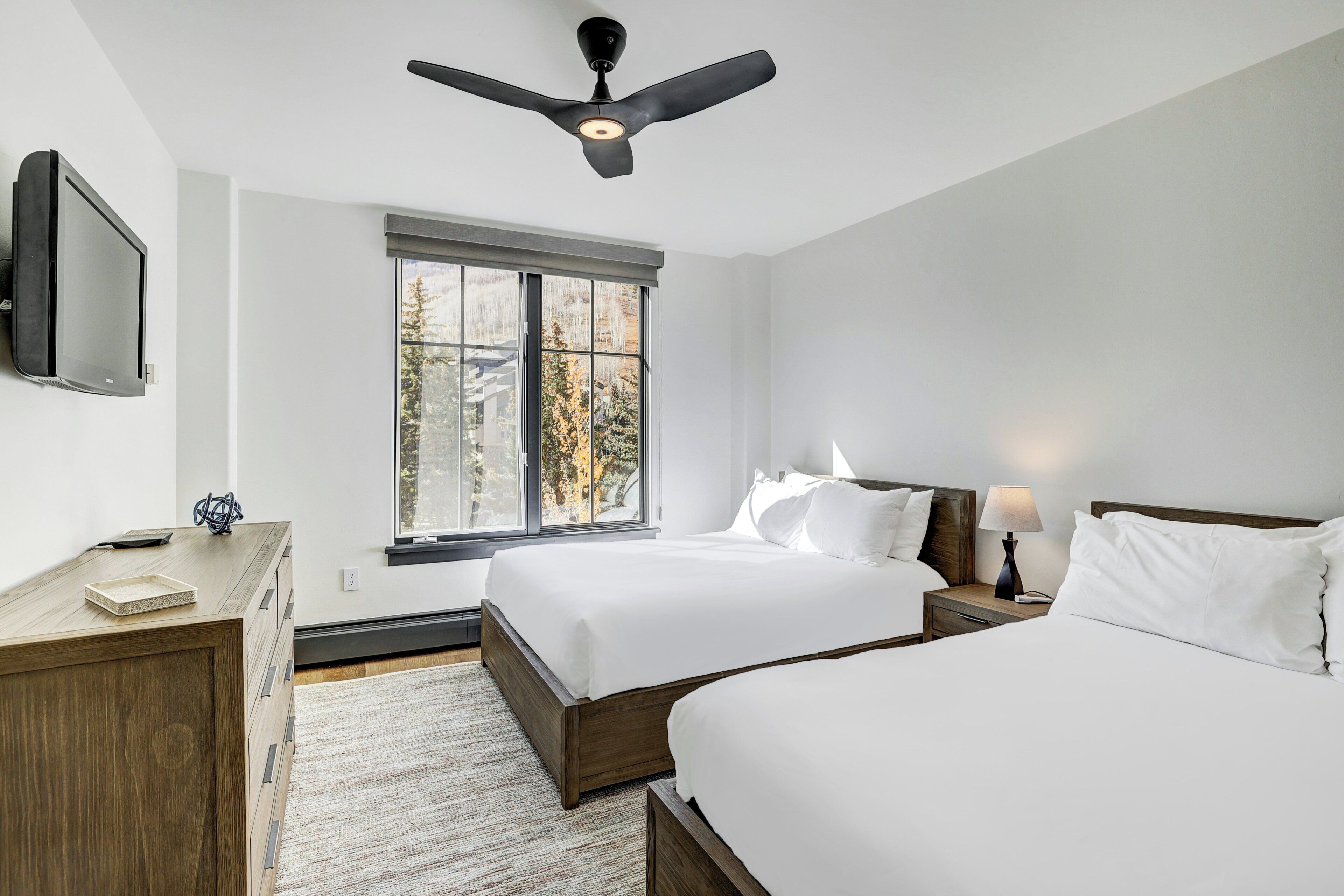 Ein modernes Hotelzimmer mit zwei Betten, einem Deckenventilator, einem großen Fenster und einem Flachbildfernseher.