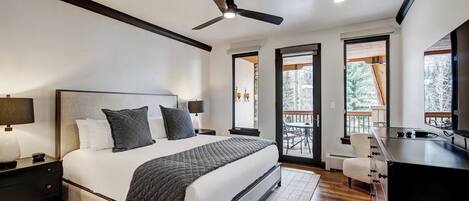 A modern bedroom with a large bed, a ceiling fan, and a view of the outdoors.